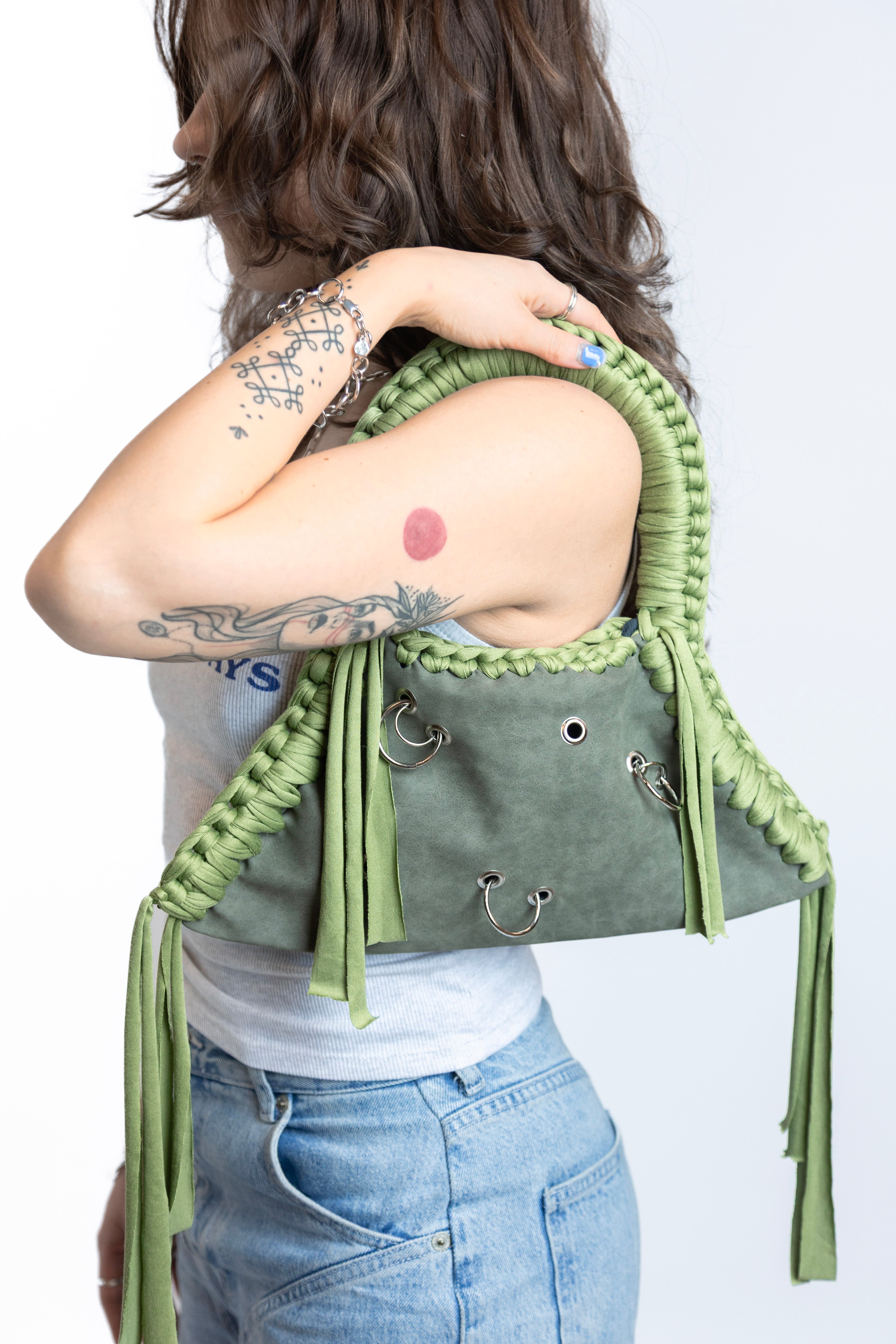 Person holding a green and gray handbag with decorative straps on a white background